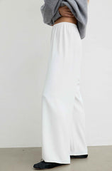 White wide-leg trousers worn by a model, styled with a gray cropped sweater and black flats, shown from the waist down against a plain light gray wall.