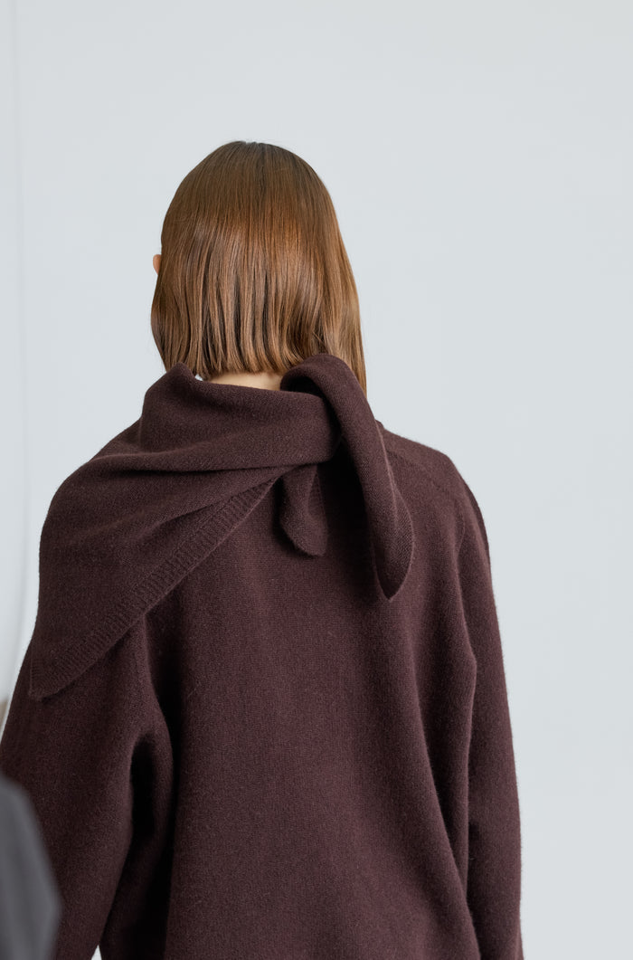 Woman wearing a dark brown scarf over a brown outfit on a light grey background
